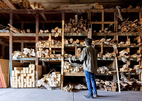 Rear view of a Latin American worker looking at logs of wood while working at a lumberyard and taking inventory