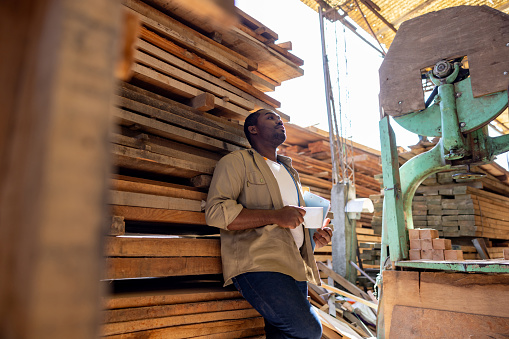 Tired African American worker relaxing on his coffee break at a lumberyard - people at work concepts
