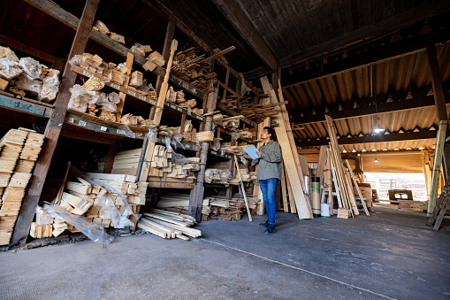 Latin American employee taking inventory on some timber at a lumberyard and writing on a clipboard