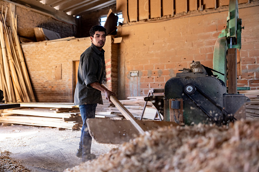 Latin American man working at a lumberyard picking up sawdust with a shovel - timber industry concepts