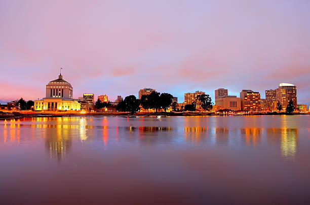 Oakland California Downtown Oakland skyline along the banks of Lake Merritt at dusk. Oakland is a major West Coast port city in the U.S. state of California in the county seat of Alameda County.  Oakland has gained recognition as a travel destination for its excellent restaurants, music venues and artist communities oakland california stock pictures, royalty-free photos & images