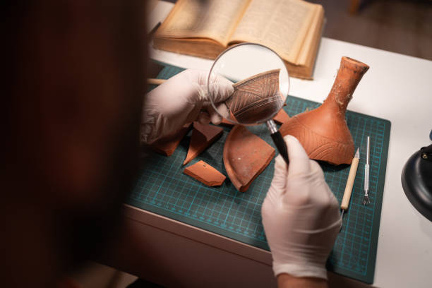 istock Archeologist working late night in office studying artifact with magnifying glass, close-up. 1755085011