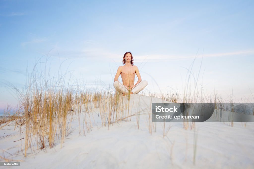 healthy man joven Meditando en la playa mientras se distiende en la arena - Foto de stock de 20 a 29 años libre de derechos