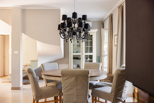 Dinning room of a villa in Istria with a small round table and a pendant light over it. The interior is in muted and beige colours. The dinning table and chair are located near a a big panoramic window.
