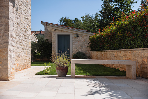 Beautiful driveway and backyard of a big Istrian Villa made out of stone. There is a beautiful concrete bench by the green grass. Beautiful Mediterranean architecture. Vacation villa in Croatia.