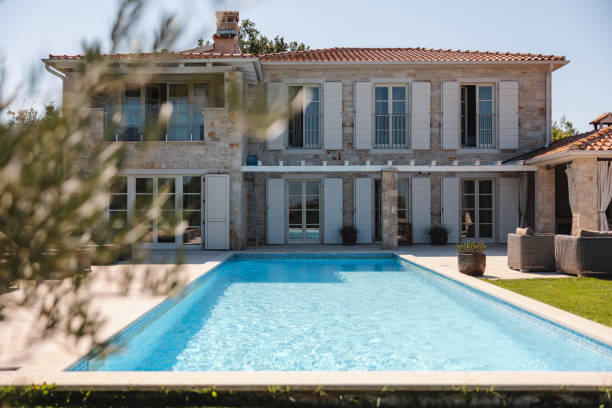 A beautiful villa in Istria with a large pool in the backyard. The sun is shining and illuminating the poolside and the beautiful stone exterior of the building. Charming vacation rental in Croatia with lots of windows. The windows have white shutters on them.