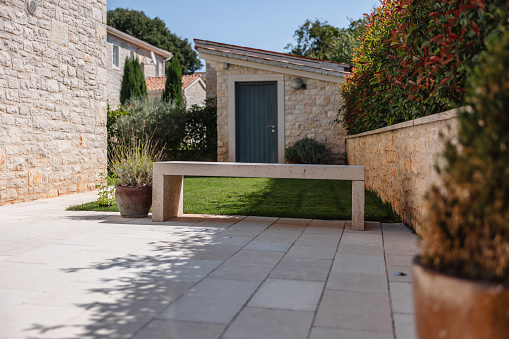 Beautiful driveway and backyard of a big Istrian Villa made out of stone. There is a beautiful concrete bench by the green grass. Beautiful Mediterranean architecture. Vacation villa in Croatia.