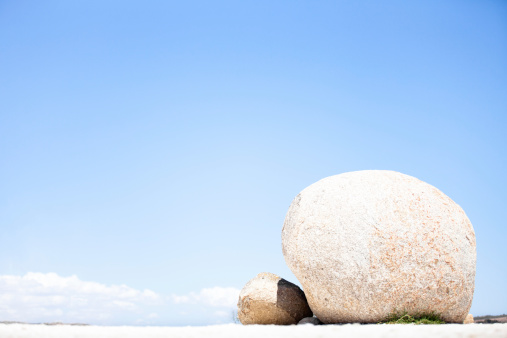 A solitary rounded white boulder sits in a sea of white sand shading a smaller boulder that sits in front of it.