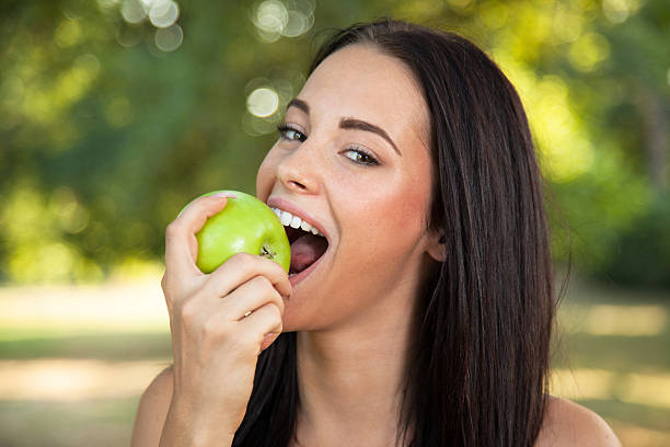 красивая молодая женщина держит кусать fresh apple, на открытом воздухе - beauty in nature women beautiful human teeth стоковые фото и изображения