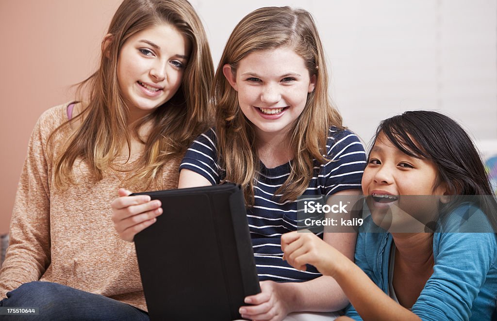 Tween girls on bed using digital tablet Multi-ethnic preteen girls (12 years) sitting in bedroom using digital tablet.  Main focus on girl in middle and Asian girl. 12-13 Years Stock Photo