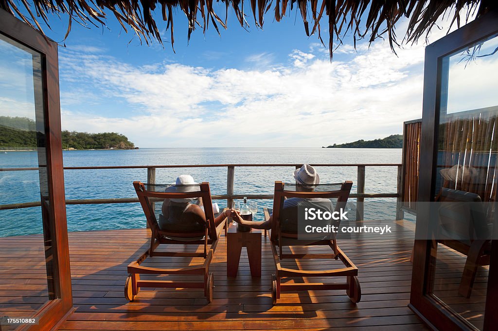 Couple dans les chaises en bois pelouse admirant l'eau - Photo de Vacances libre de droits