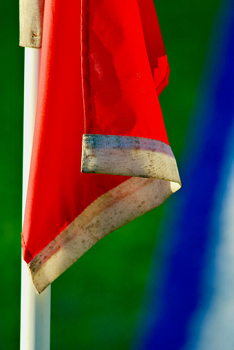 Afternoon sun bathes a red flag that marks the corner of a soccer field used for soccer competitions.