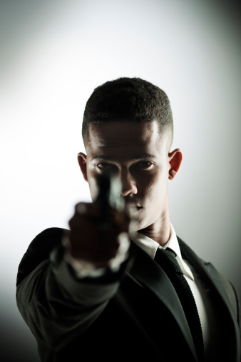 One young man holding a handgun. He is formally dresses in a dark background. More files of this model and theme on port. Horizontal composition.