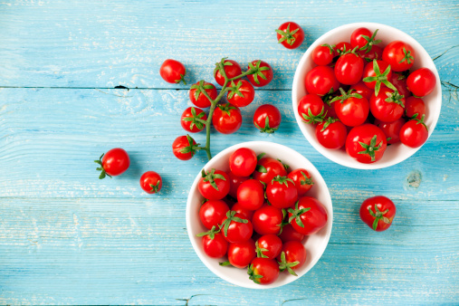 Fresh cherry tomatoes in bowls on wooden table