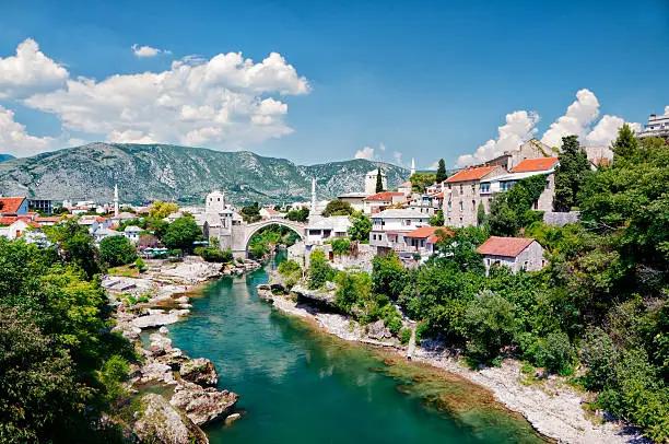 "Old Arc bridge in Mostar, Bosnia and Hercegovina. Destroyed during the war. It was then rebuild after the war. Beautiful cityscape of Mostar, visible are traditional architecture of Bosnia, many green trees and cumulus clouds over Neretva River.See more images like this in:"