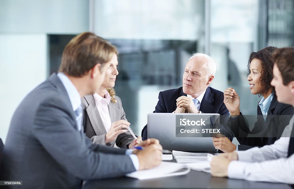 Listening to an interesting proposal Focused executives sitting at a table during a meeting and using a laptop Business Person Stock Photo