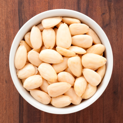 Top view of white bowl full of peeled almonds