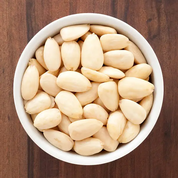 Top view of white bowl full of peeled almonds