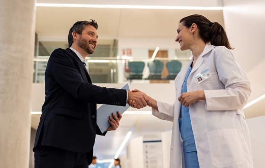 Health insurance agent handshaking with a doctor at the hospital - healthcare and medicine concepts