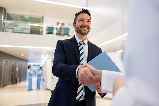 Happy pharmaceutical salesman handshaking with a doctor at the hospital - healthcare and medicine concepts
