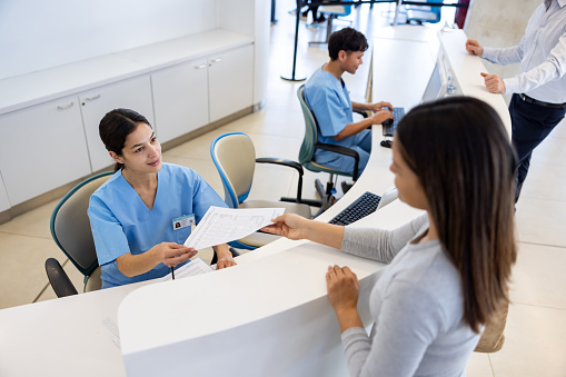 Patient handing a form to a nurse at the front desk of the hospital - healthcare and medicine concepts