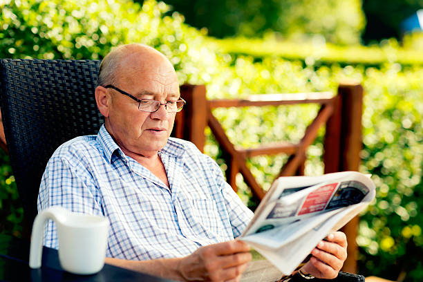Senior man is reading a newspaper outside