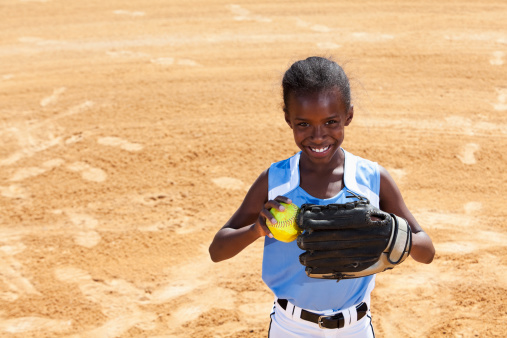 African American girl (9 years) playing softball, standing on pitcher's mound.