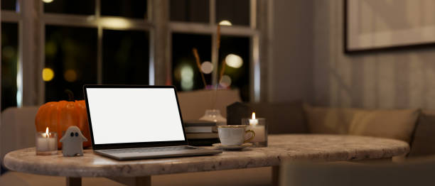 istock Home workspace at night in a Halloween theme, a white-screen laptop mockup on a table in a room. 1755191401