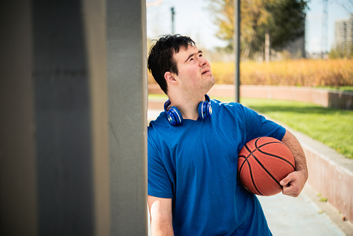 Happy young man with down syndrome playing basketball outside