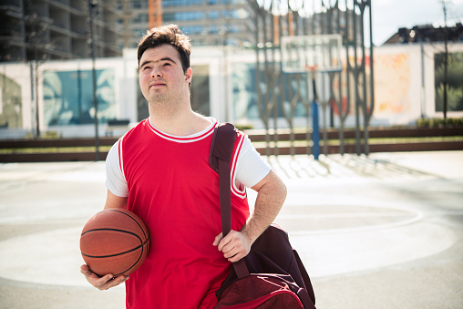 Happy young man with down syndrome playing basketball outside