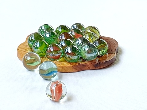 A collection of well used colorful glass marbles from  children's play in the pas in a shallow yellow bowl. .
