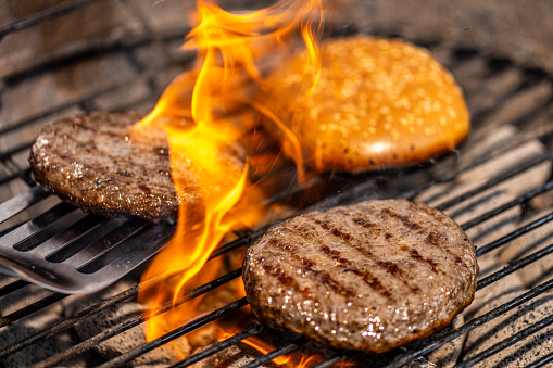 Close-up of beef burger patties getting roasted together with burger bread on a charcoal barbecue grill.