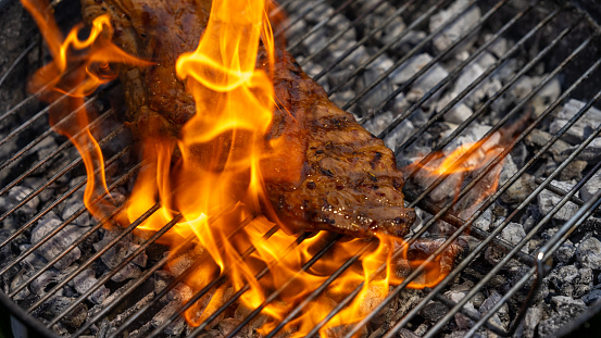 Piece of pork engulfed in flames roasting on a wire grid of a charcoal barbecue grill.