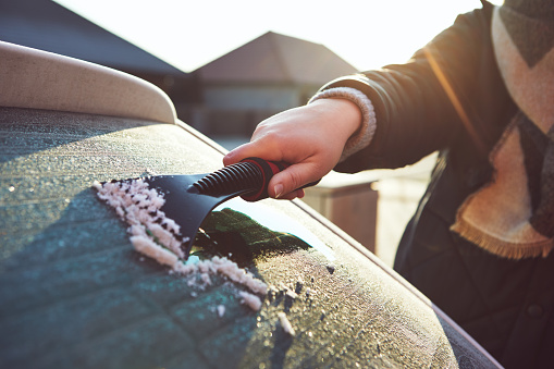 A woman scrapes frost off the front window of her car on a cold winter morning