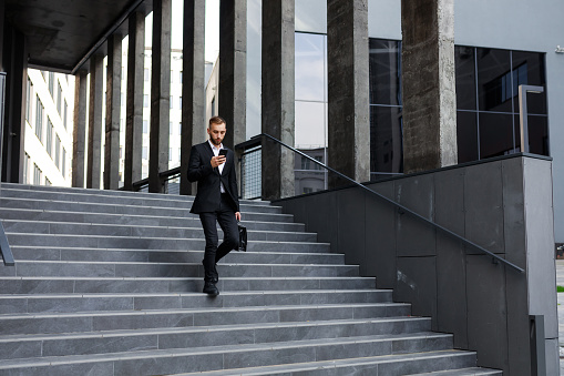 Young successful businessman going down the staircase and using smart phone for text message.