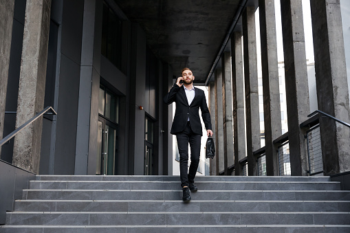 Young handsome businessman walking down stairs talking on the phone