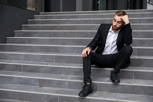 Image of a pensive businessman sitting on the stairs near the office building.