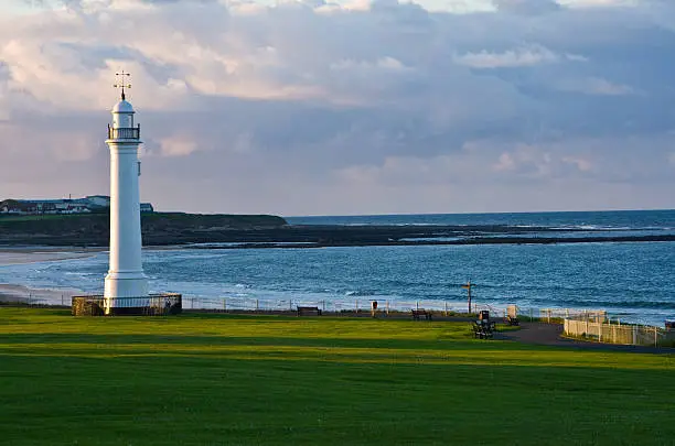The seafront in Sunderland just before sunset in early summer showing the old lighthouse which used to stand on the south pier before being moved to Seaburn. In the distance is Whitburn. The light is naturally yellow with strong long shadows.