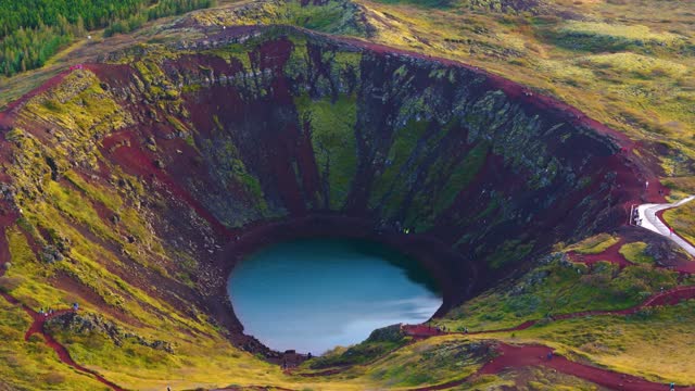 Kerid crater in Iceland, water at the bottom, red earth, vegetation and a fir forest in the background
