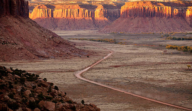 Car speeding down dusty desert road in Utah at sunset