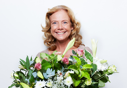 Pretty senior woman holding a bunch of flowers while isolated on white