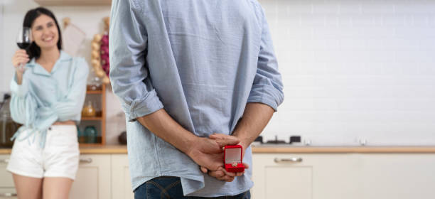 집 부엌에서 로맨틱한 저녁 식사를 하는 다민족 커플. 한 남자가 결혼 반지가 끼인 상자를 들고 서 있습니다. -   brunette  뉴스 사진 이미지