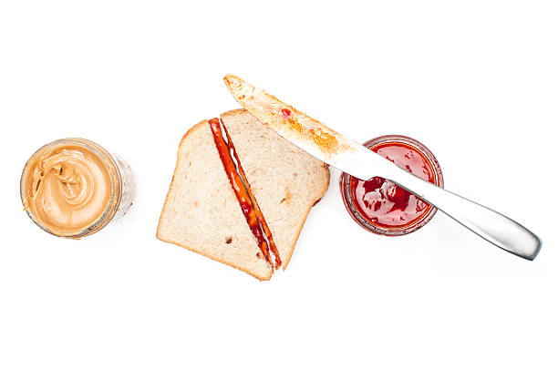 PB&J sandwich between jars of peanut butter and jelly with knife on jelly jar. Isolated on white.