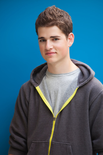 Handsome teenager standing in front of a blue background.