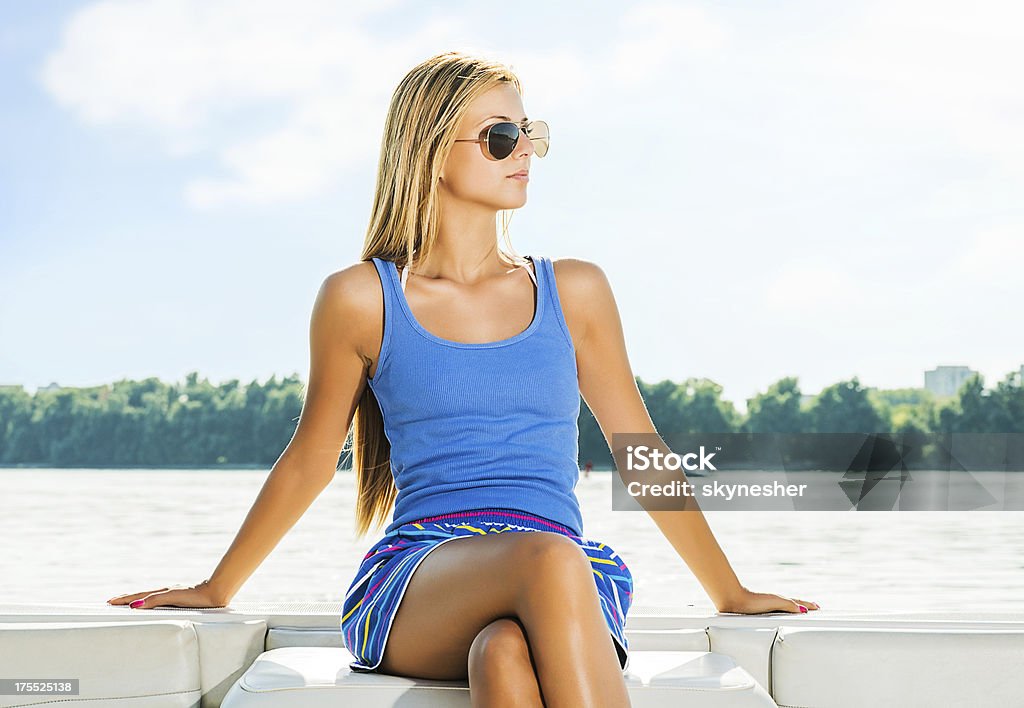 Beautiful blonde woman sitting on the boat. Attractive young blonde woman sitting on the edge of the speed boat and looking at distance. Speedboat Stock Photo Beautiful blonde woman sitting on the boat. Attractive young blonde woman sitting on the edge of the speed boat and looking at distance. Speedboat Stock Photo