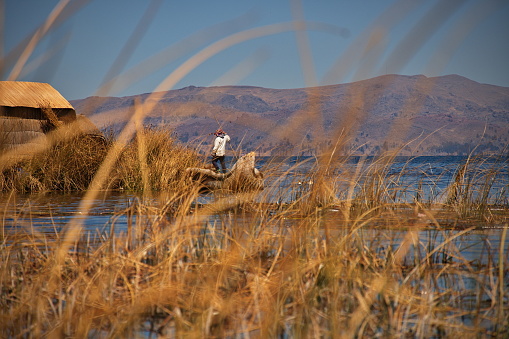 Uros man on a reed boat next to his floating island on Lake Titicaca