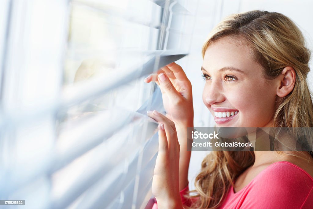 Getting excited for the day ahead! A beautiful young woman looking out at the day through a window Window Blinds Stock Photo