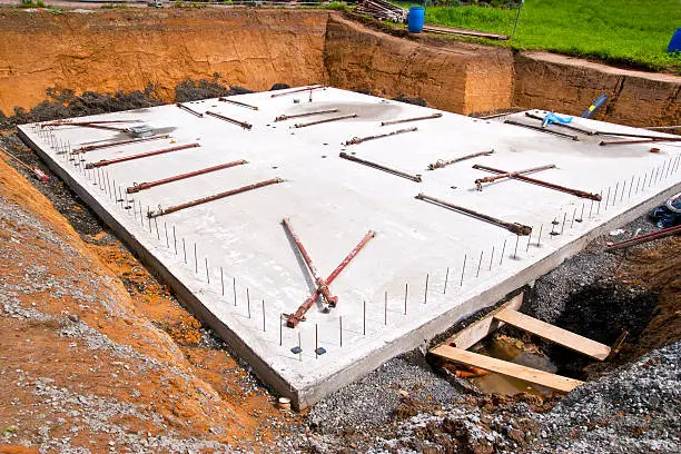 "Concrete foundation, floor of the basement for a new home, reinforcing steel on the edges for installation of precast concrete walls, on ground lying pillars to keep the walls up to the final assembly."