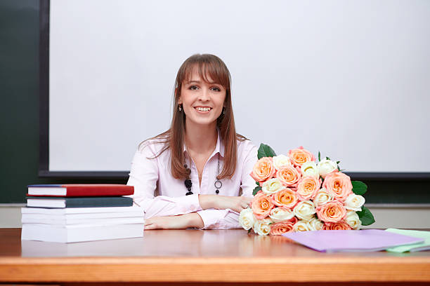 Smiling teacher with books and flowers.