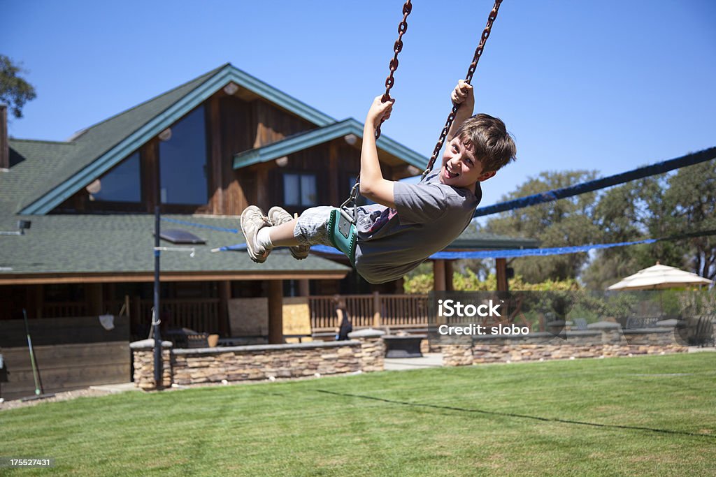 Swing in a front yard Young boy on a swing in front of big log house. 10-11 Years Stock Photo